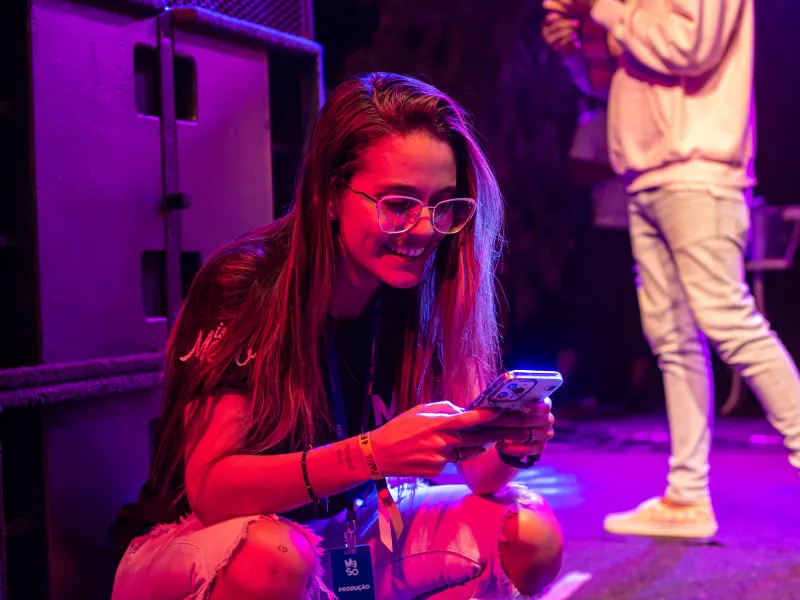 Marina Moura agachada nos bastidores de um show, olhando para o celular