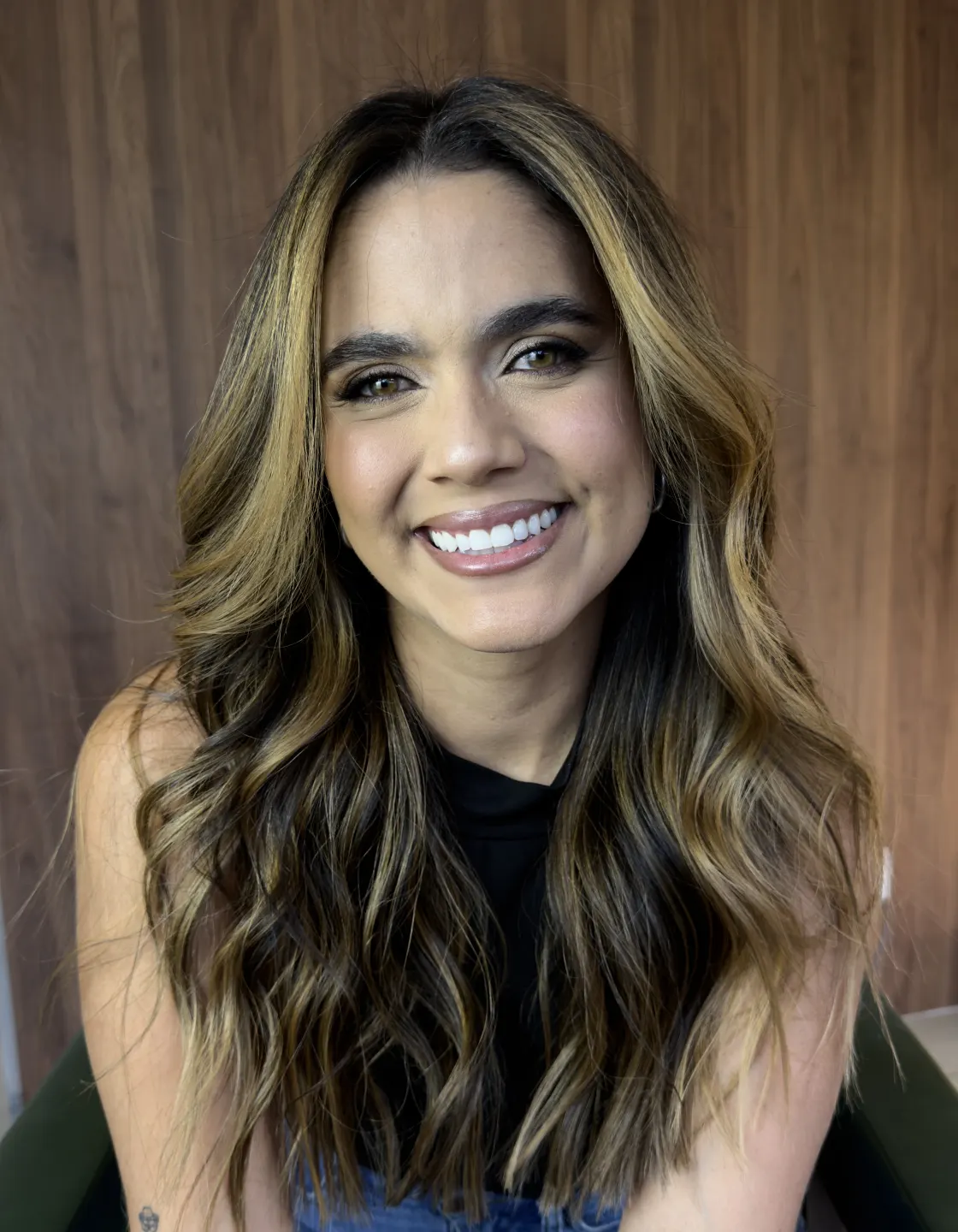 Marina Moura sorrindo, sentada diante de uma parede de madeira